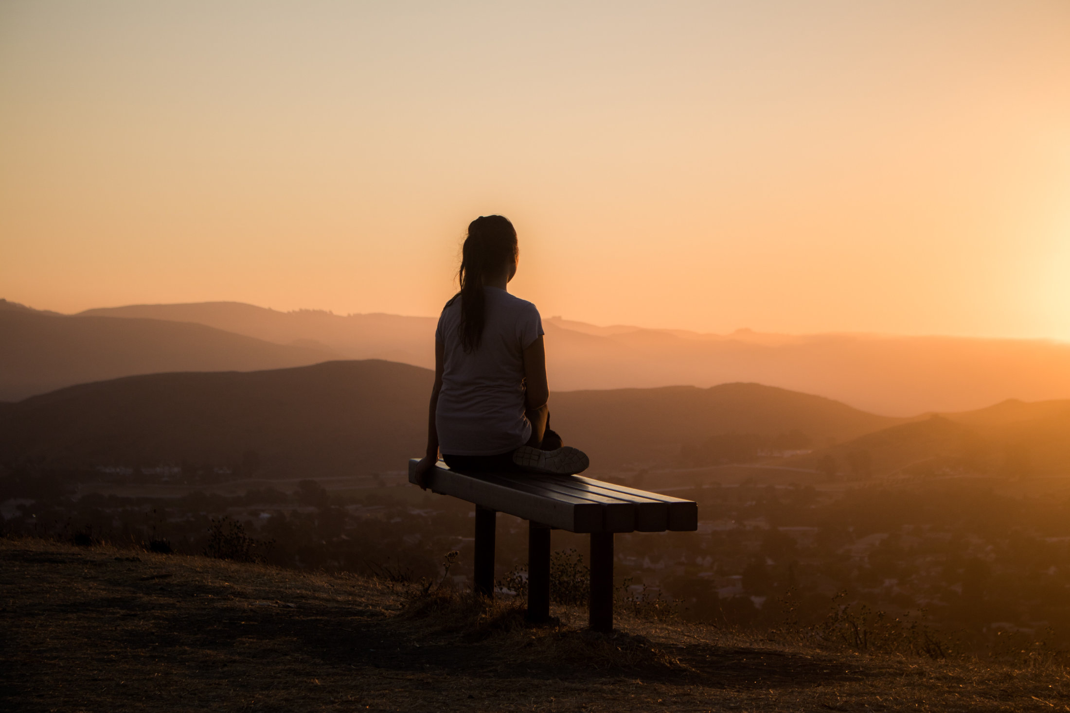 Woman on bench at sunset relaxing for stress reduction.