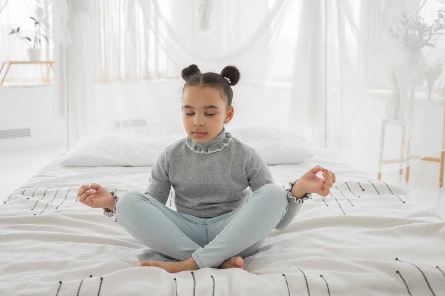 Girl sitting on the bed with legs crossed and hands out in meditation.